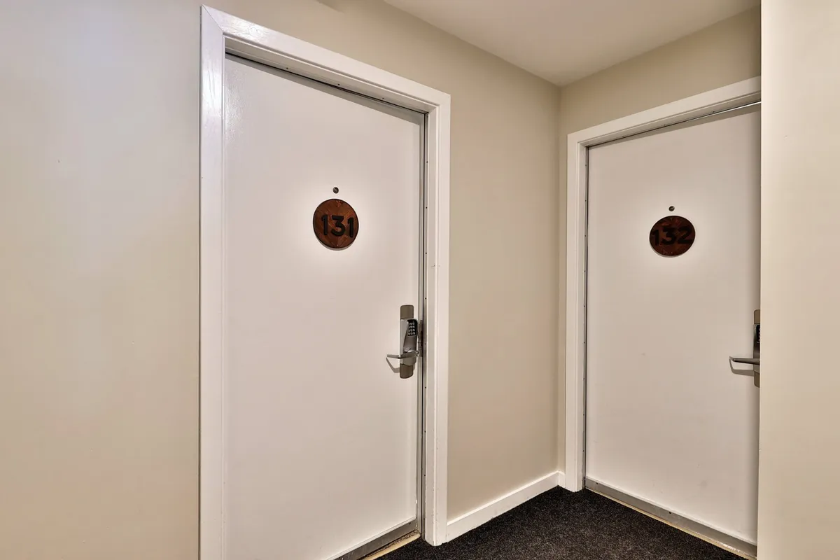 This image shows two numbered doors (131 and 132) in an interior hallway, suggesting the entryway to private accommodations. The neutral mood and simple hallway scene create a sense of arrival and privacy.