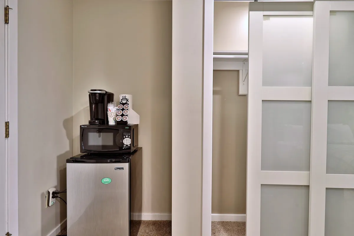 A functional kitchenette corner is visible, showcasing the mini fridge, microwave, and Keurig coffee maker on the countertop. The setup is clean and inviting, emphasizing the flexibility and convenience for preparing snacks, brewing coffee, or storing refreshments.