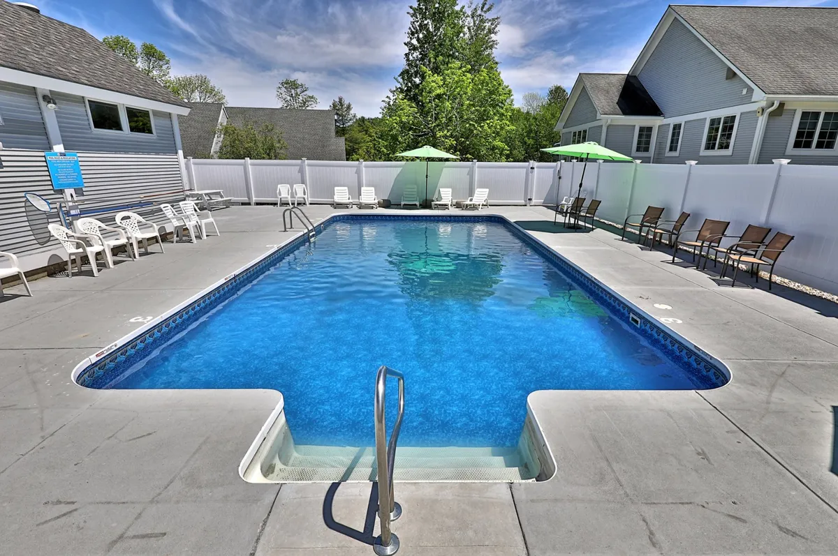This inviting exterior shot showcases the heated saltwater swimming pool surrounded by lounge chairs and umbrellas, all nestled within lush greenery. The scene radiates a leisurely, cheerful mood, hinting at the relaxing and social atmosphere the property offers during summer months.