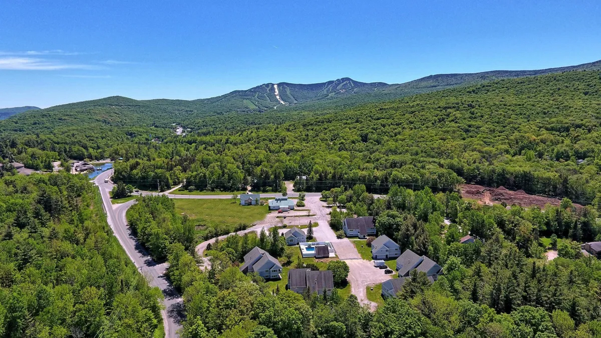 A sweeping exterior view captures a Vermont mountain range with vibrant autumn foliage, a winding road, and scattered homes nestled among the trees. The tranquil landscape alludes to outdoor activities such as hiking, biking, and exploring the natural beauty surrounding the property.